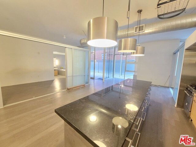 kitchen featuring wood-type flooring, high end stainless steel range, hanging light fixtures, and dark stone counters