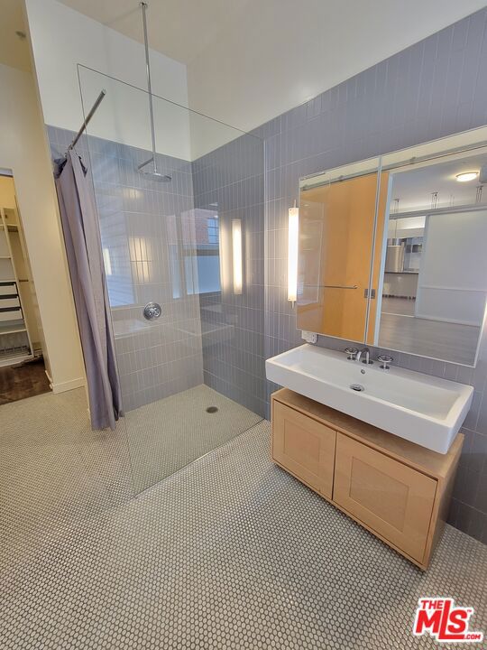 bathroom featuring a tile shower, vanity, tile patterned floors, and tile walls