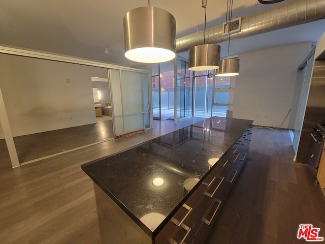 kitchen with pendant lighting, dark hardwood / wood-style floors, dark stone countertops, and a center island