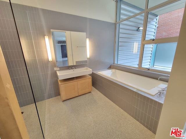 bathroom with a relaxing tiled tub, vanity, and tile patterned flooring