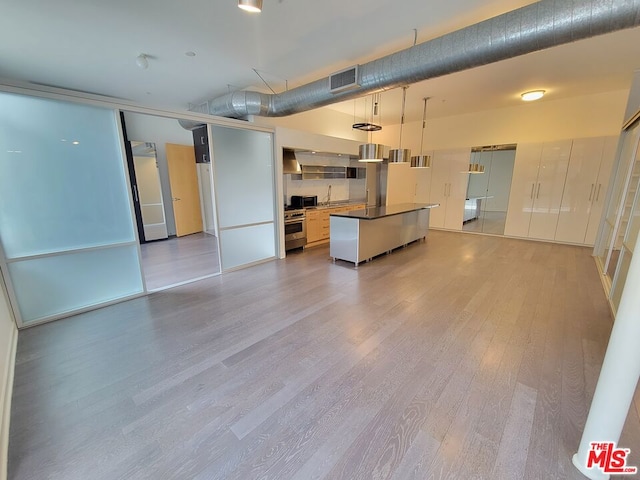 kitchen with pendant lighting, white cabinetry, a center island, high end stainless steel range, and light wood-type flooring