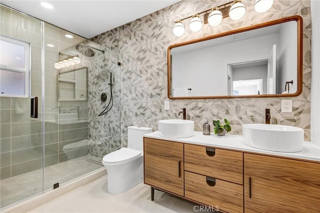 bathroom with vanity, toilet, a shower with shower door, and tile walls