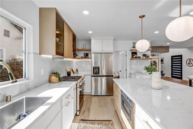 kitchen featuring sink, stainless steel appliances, decorative light fixtures, white cabinets, and light wood-type flooring