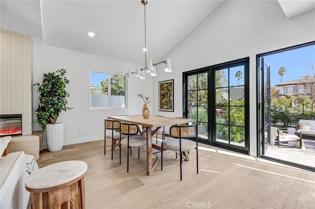 dining area with a large fireplace, high vaulted ceiling, and light wood-type flooring