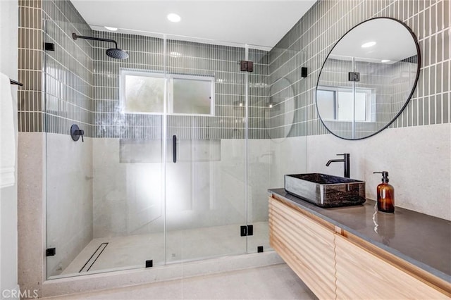 bathroom featuring a shower with door, vanity, and tile walls