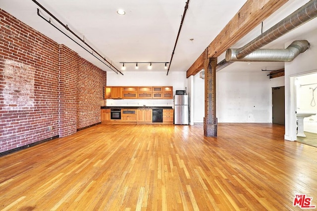 unfurnished living room featuring rail lighting, light hardwood / wood-style floors, and brick wall