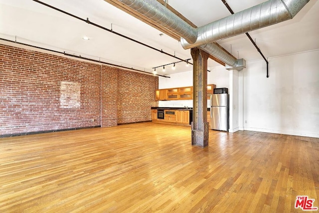 unfurnished living room with light hardwood / wood-style flooring and brick wall