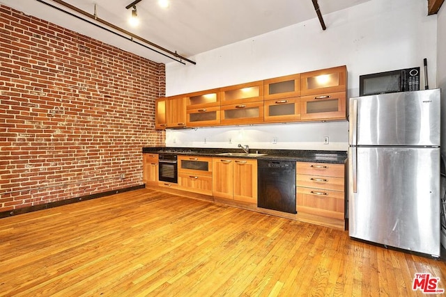 kitchen with black appliances, sink, dark stone countertops, light hardwood / wood-style floors, and brick wall