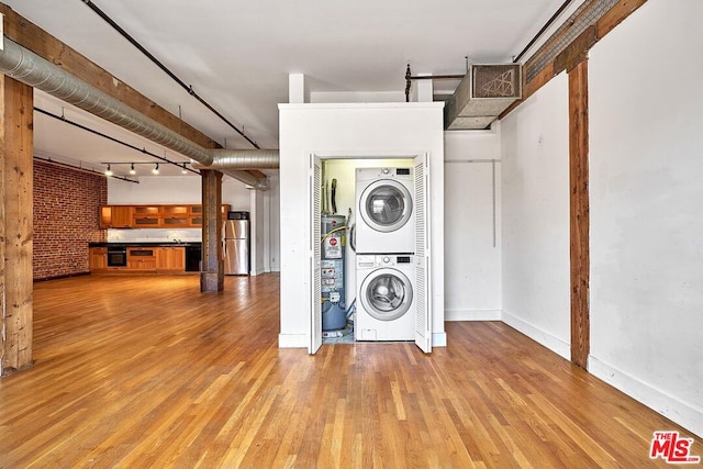 clothes washing area featuring light wood-type flooring, track lighting, stacked washer / dryer, and water heater