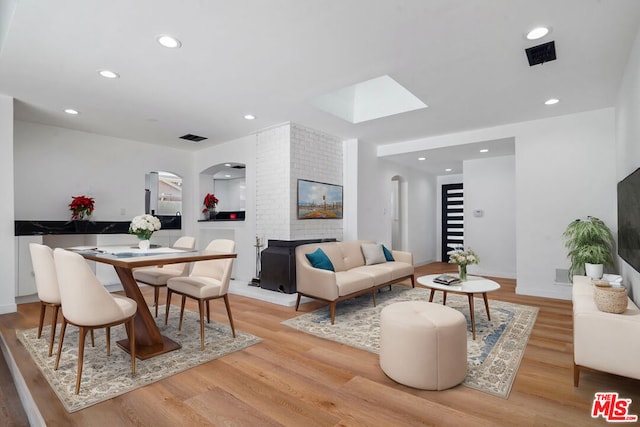 living room with a skylight, a fireplace, and light hardwood / wood-style flooring