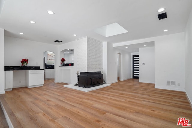 unfurnished living room featuring light hardwood / wood-style flooring, a wood stove, and a skylight