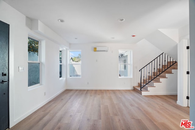 unfurnished living room featuring light hardwood / wood-style flooring and a wall mounted air conditioner