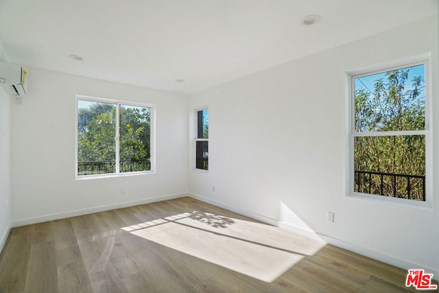 spare room featuring a wall mounted air conditioner, hardwood / wood-style flooring, and plenty of natural light