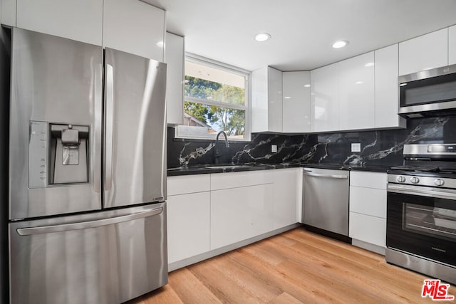 kitchen with white cabinetry, sink, tasteful backsplash, light hardwood / wood-style floors, and appliances with stainless steel finishes