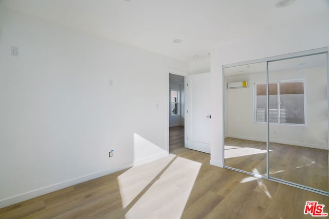 unfurnished bedroom with a closet, light hardwood / wood-style floors, and a wall mounted air conditioner