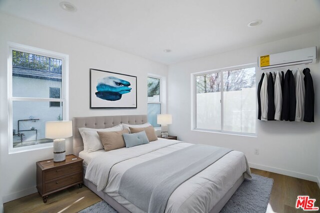 bedroom featuring hardwood / wood-style floors, a wall mounted air conditioner, and multiple windows