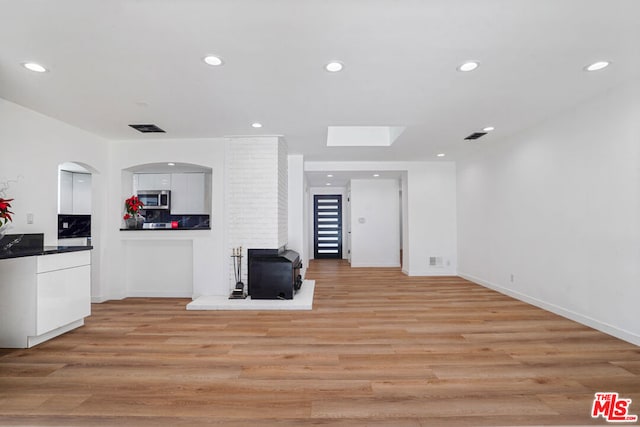 kitchen with light wood-type flooring, a skylight, tasteful backsplash, white cabinetry, and a wood stove