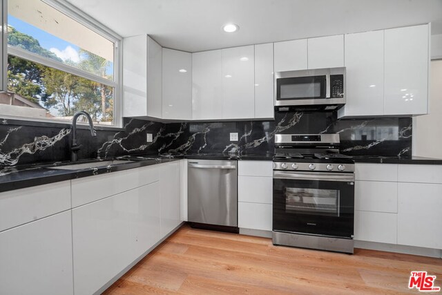 kitchen with tasteful backsplash, white cabinetry, appliances with stainless steel finishes, and light hardwood / wood-style flooring