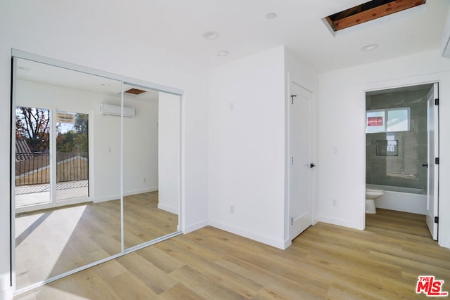 unfurnished bedroom with ensuite bathroom, access to exterior, light wood-type flooring, and a closet