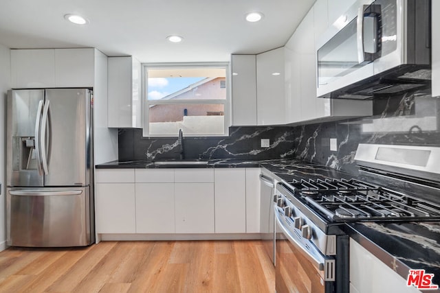 kitchen with white cabinets, tasteful backsplash, stainless steel appliances, and light hardwood / wood-style flooring