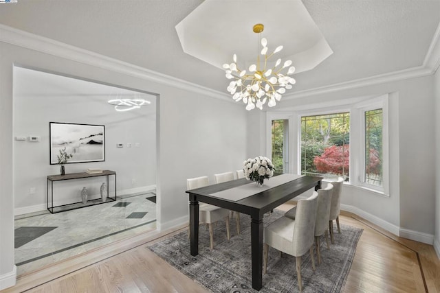 dining area featuring a raised ceiling, a notable chandelier, ornamental molding, and light hardwood / wood-style floors