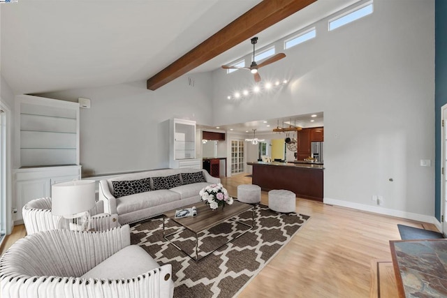 living room with ceiling fan, a towering ceiling, light hardwood / wood-style flooring, and beamed ceiling