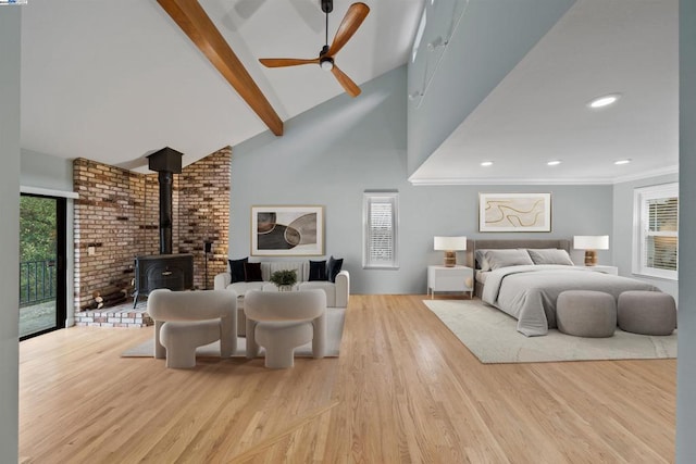 bedroom with ceiling fan, access to exterior, beamed ceiling, light hardwood / wood-style flooring, and a wood stove