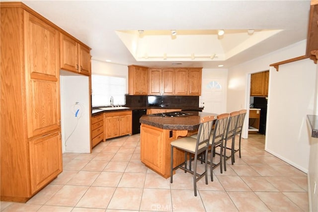 kitchen with dishwasher, sink, a tray ceiling, a kitchen bar, and a kitchen island