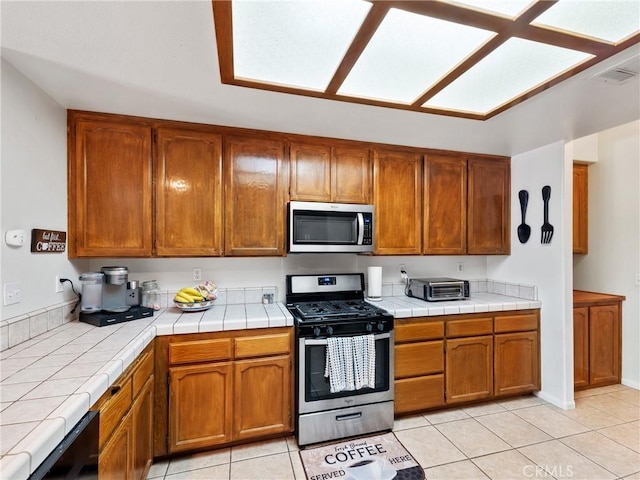 kitchen with tile counters, light tile patterned floors, and appliances with stainless steel finishes