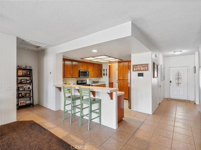 kitchen featuring a textured ceiling, appliances with stainless steel finishes, light tile patterned flooring, kitchen peninsula, and a breakfast bar area