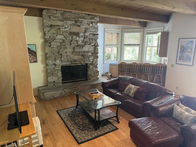 living room featuring light wood-type flooring, wooden ceiling, a stone fireplace, and beamed ceiling