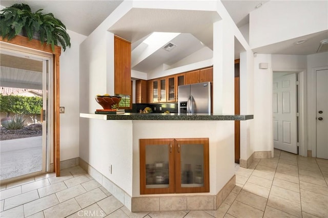 kitchen with light tile patterned floors, stainless steel fridge with ice dispenser, kitchen peninsula, and vaulted ceiling