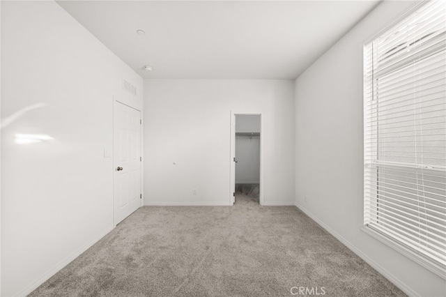 unfurnished bedroom with light colored carpet, a spacious closet, and a closet