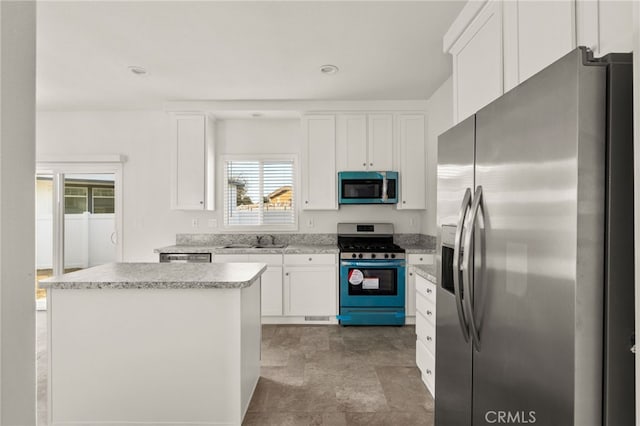 kitchen with appliances with stainless steel finishes, white cabinetry, a kitchen island, and sink