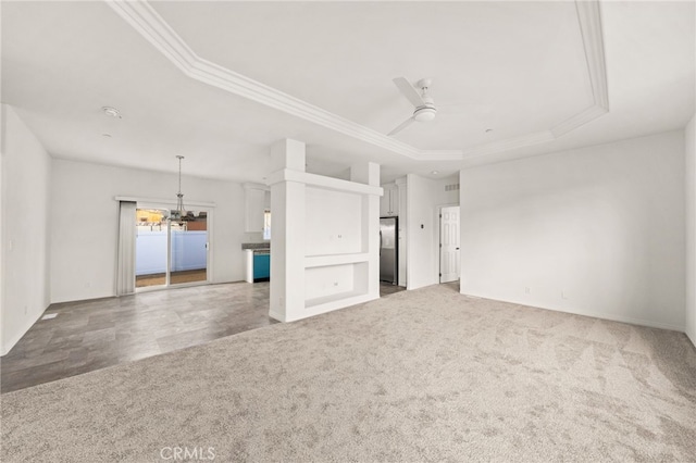 unfurnished living room featuring carpet floors, ceiling fan with notable chandelier, a tray ceiling, and ornamental molding