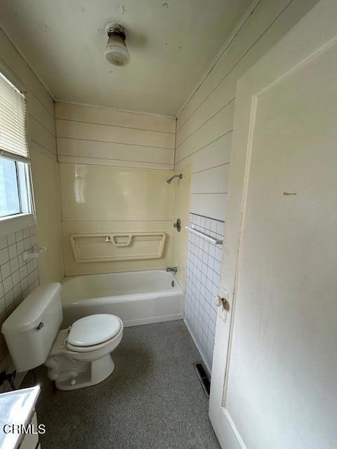 full bathroom featuring shower / bath combination, toilet, vanity, and wood walls