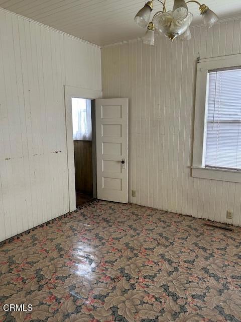 spare room with wood walls and a notable chandelier