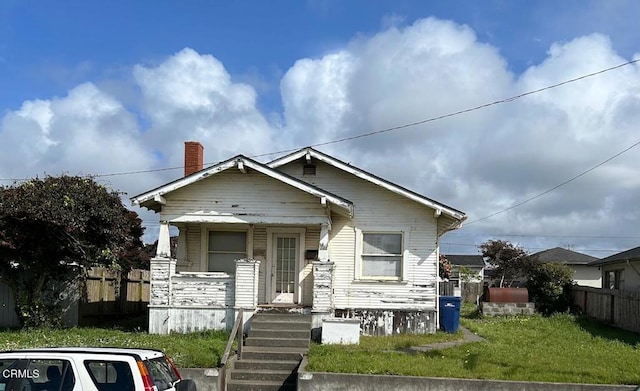 bungalow-style home with a chimney, fence, a porch, and a front yard