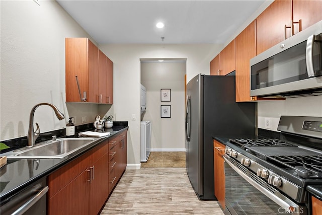 kitchen with sink, light wood-type flooring, stacked washer and clothes dryer, and appliances with stainless steel finishes