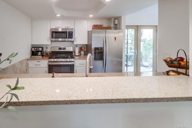 kitchen with white cabinets, appliances with stainless steel finishes, kitchen peninsula, and light stone counters