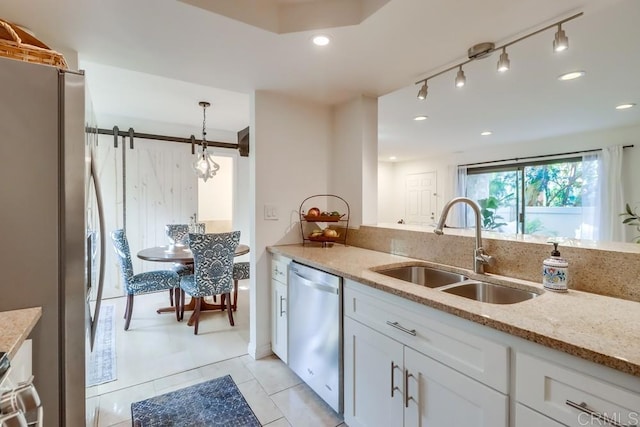 kitchen with white cabinetry, sink, light stone countertops, a barn door, and appliances with stainless steel finishes