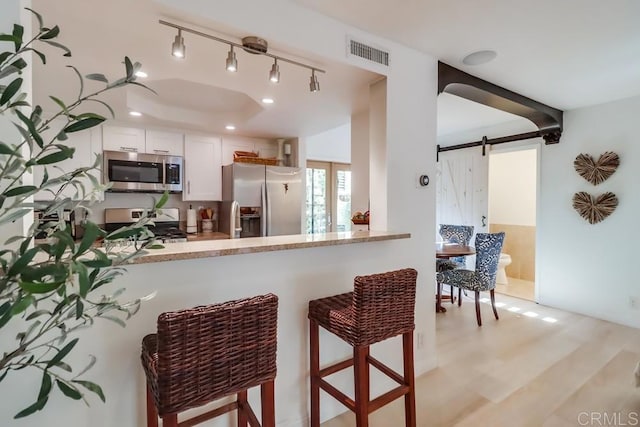 kitchen featuring a barn door, kitchen peninsula, white cabinets, and appliances with stainless steel finishes