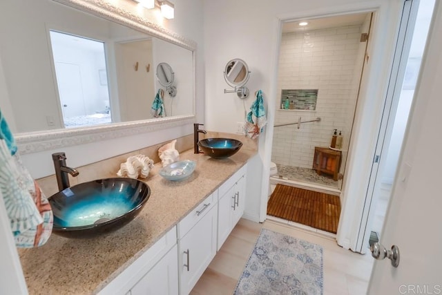 bathroom featuring toilet, tile patterned flooring, vanity, and tiled shower