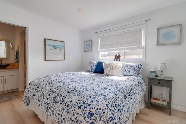 bedroom with connected bathroom, multiple windows, sink, and light hardwood / wood-style floors