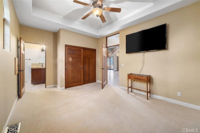 carpeted bedroom with ceiling fan, a tray ceiling, a closet, and ensuite bath