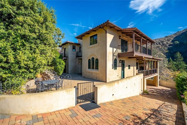 rear view of house with a balcony, a garage, a patio area, and a mountain view