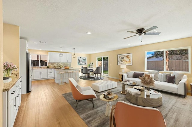 living room featuring ceiling fan, a textured ceiling, and light hardwood / wood-style flooring