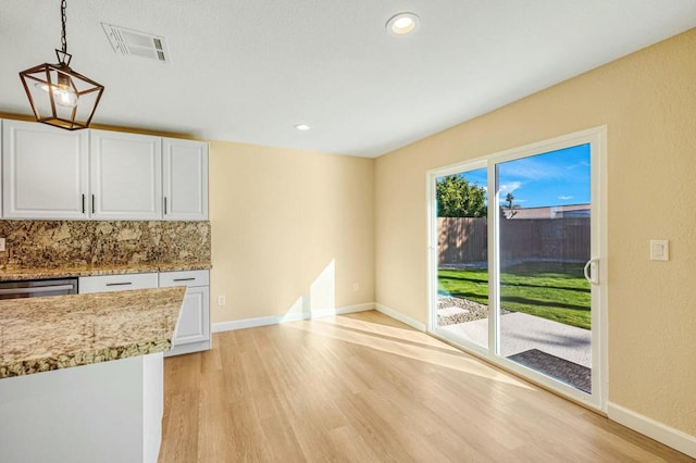 kitchen featuring hanging light fixtures, white cabinets, tasteful backsplash, and light hardwood / wood-style floors