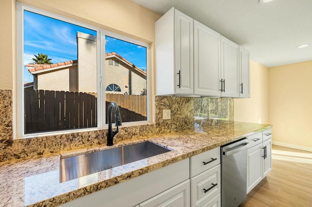 kitchen with sink, white cabinetry, stainless steel dishwasher, and light wood-type flooring