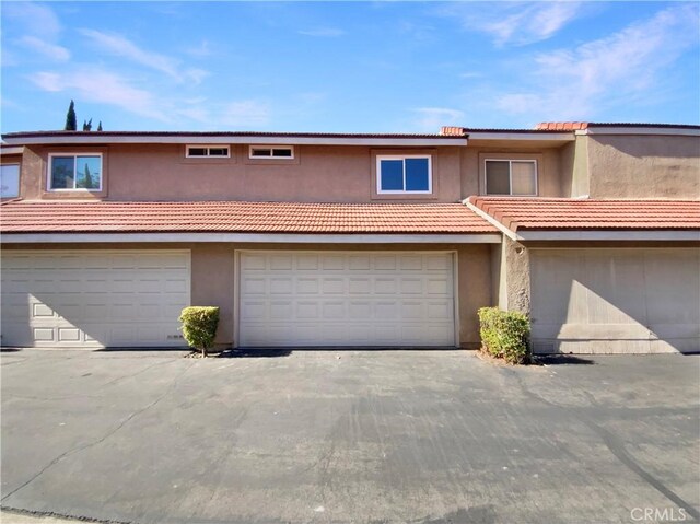 townhome / multi-family property with stucco siding, a tiled roof, and a garage